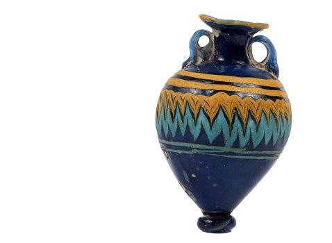 An ancient, dark blue glass amphora with ochre and turquoise zigzag patterns, featuring two handles. The design is intricate and vibrant.