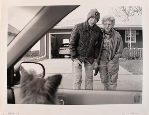 black and white photo of an older couple looking through a car window at a small dog